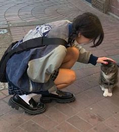 a woman kneeling down petting a cat on the street