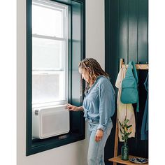 a woman standing in front of a window looking at something on the wall next to her