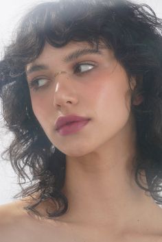 a close up of a woman with curly hair and blue eyes wearing a gold nose ring