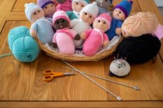 a basket filled with lots of knitted dolls next to yarn balls and knitting needles