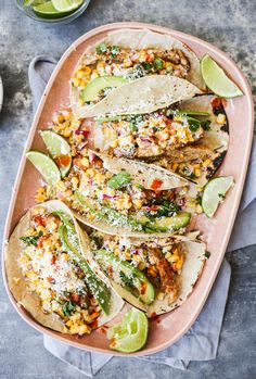 several tacos on a pink platter with lime wedges and cilantro