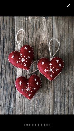 three red hearts with white stars hanging from strings on a wooden surface, ready to be used as ornaments