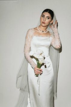 a woman in a white wedding dress holding a flower and wearing a veil with her hand on her head