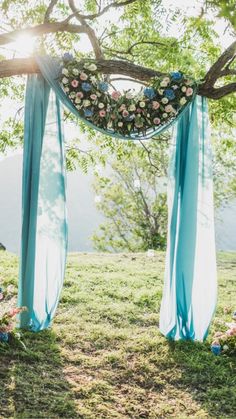 an outdoor ceremony with blue draping and flowers on the arch, surrounded by greenery