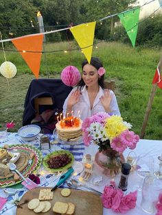 a woman sitting in front of a cake with lit candles on it at a picnic table