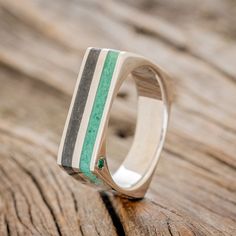 a wooden ring with green, black and white stripes on the outside of it sitting on top of a piece of wood