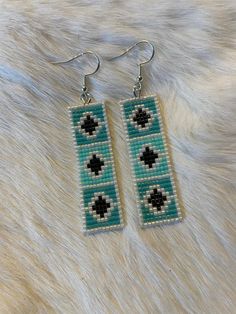 a pair of earrings made out of seed beads on top of a white fur surface