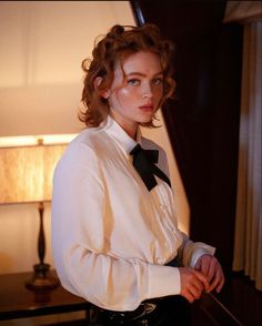 a woman wearing a white shirt and black bow tie standing in front of a lamp