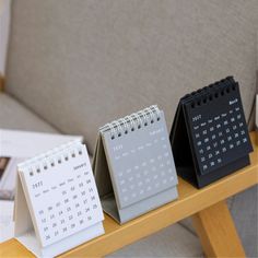 three desk calendars sitting on top of a wooden table next to a gray couch