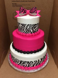 a three tiered cake decorated with zebra print and pink ribbon, sitting in a cardboard box