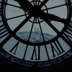 a large clock with roman numerals in front of a cityscape behind it