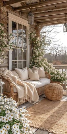 a porch with wicker furniture and flowers on the floor, along with white daisies