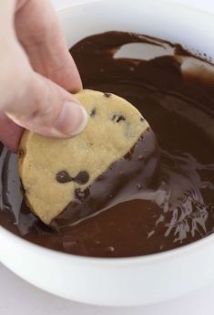 someone dipping a cookie into melted chocolate in a bowl