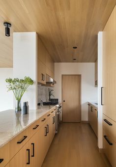 a long narrow kitchen with wooden cabinets and white marble counter tops, along with a vase filled with flowers