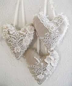 two heart shaped ornaments hanging from strings on a white surface with lace and pearls around them