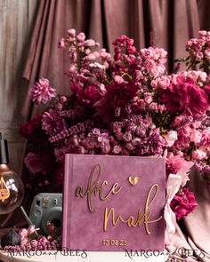 a pink box with gold lettering on it next to flowers