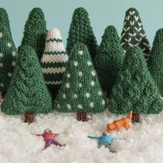 small knitted christmas trees are lined up in the snow, and one is holding an ornament