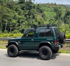 a green jeep is parked on the side of the road with trees in the background