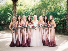 a group of women standing next to each other in front of trees and bushes holding bouquets