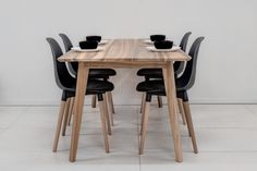 a wooden table topped with black chairs next to a white wall