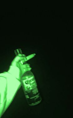 a person holding a bottle in the dark with green light on it's side