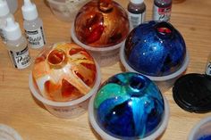 there are many different colored balls on the table with paint bottles around them and one is empty