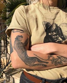 a woman with her arms crossed and tattoos on her chest is standing in front of an iron fence