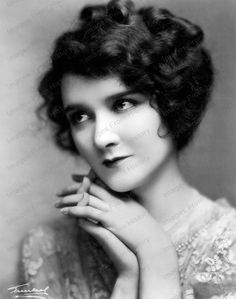 an old black and white photo of a woman with her hand on her chin looking at the camera