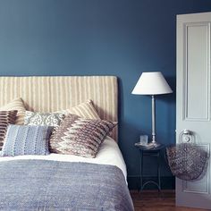 a bedroom with blue walls and wooden flooring is pictured in this image, the bed has two pillows on it