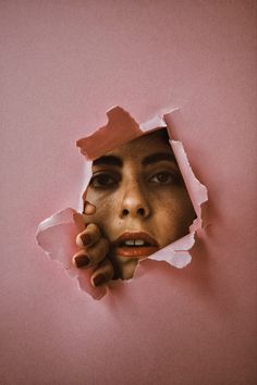 a woman's face peeking through a torn piece of paper with her hand on her cheek