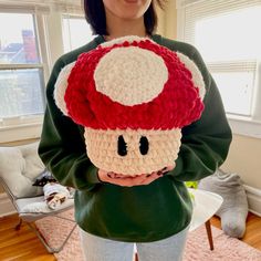 a woman holding up a crocheted mushroom hat