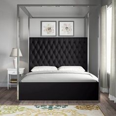 a bed with a black headboard and white sheets in a room next to a window