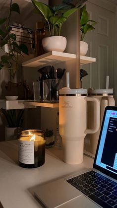 an open laptop computer sitting on top of a white desk next to a candle and potted plant