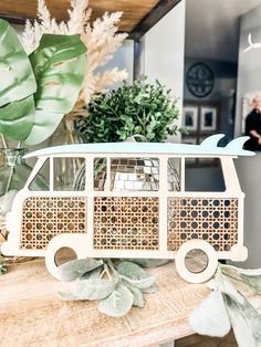 a small wooden bus sitting on top of a table next to plants and potted plants