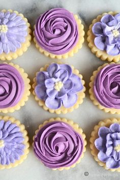 purple and yellow cupcakes decorated with flowers on a marble table top, ready to be eaten