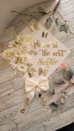 a white graduation cap with gold lettering and flowers on the front, sitting on a wooden floor