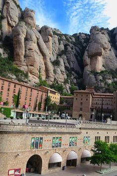 the mountains are covered with rock formations and buildings in front of them, while people walk on the sidewalk below