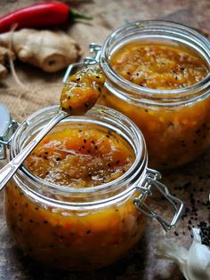 two glass jars filled with food sitting on top of a table next to garlic and pepper