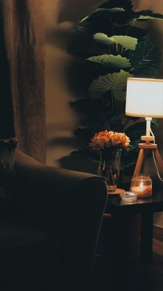 a lamp on a table next to a chair with a plant in the corner behind it