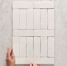 two hands are placing white tiles on top of each other to make a wall decoration