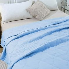 a bed with blue comforter and pillows on top of it next to a night stand