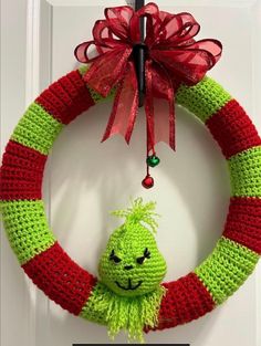 a green and red knitted wreath with a smiling face hanging from the front door