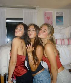 three beautiful young women standing next to each other in front of a bed and window