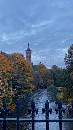 a view of a river with trees in the foreground and a clock tower in the background