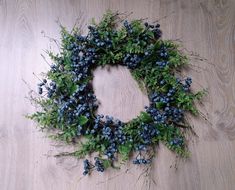 a wreath with blue berries and green leaves on a wooden surface, surrounded by wood planks