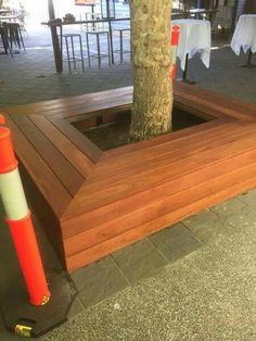 a wooden bench sitting next to a tree on top of a cement ground near tables and chairs