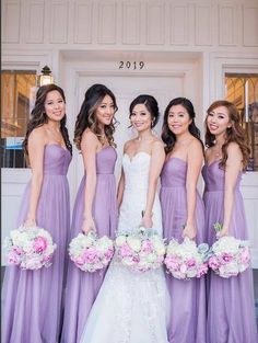 a group of women standing next to each other in front of a white door holding bouquets