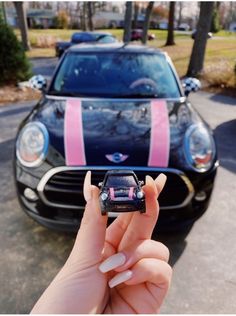 a person holding up a cell phone in front of a mini car with pink stripes