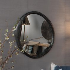 a round mirror hanging on the wall above a table with pillows and flowers in front of it