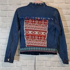 a denim jacket hanging on a white brick wall with an embroidered pattern in the back